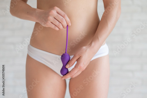 Faceless woman in white panties and with a bare tummy holds a kegel trainer. Latex vaginal vibrator for training the pelvic floor muscles with an antenna. The device for imbuilding. Women Health. photo
