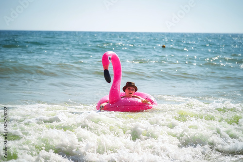 Pink inflatable flamingo. A girl is swimming in the sea. Sea waves. Cheerful mood. Vacation at the sea.