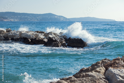 Water splashing while powerful waves crushing into the rocks in the Mediterranean sea coast with mountains on background. Nature, vacation or summer concept. High quality photo