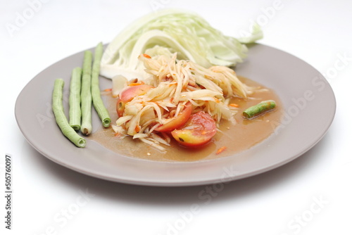 Thai papaya salad on a plate, papaya salad with poop, lime, pepper, red tomatoes in a gray plate on a white table.