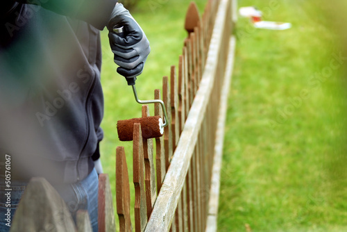 Man is painting wooden fence with brown paint outside photo