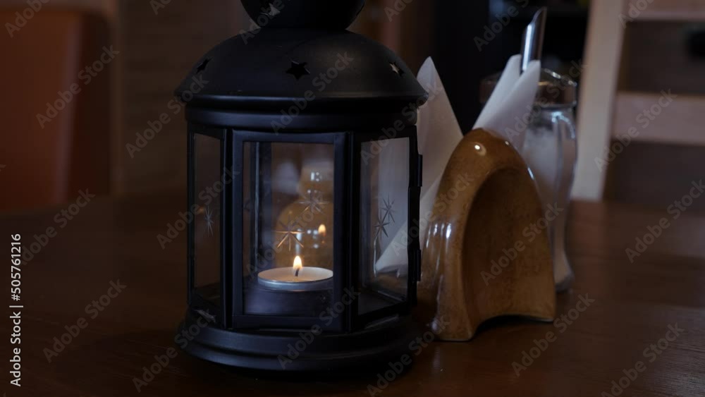 Decorative lamp with a candle inside stands on a wooden table. Decorative lamp with a candle inside stands on a wooden table.