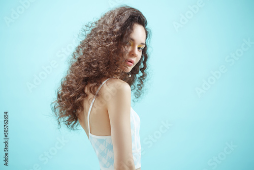 Portrait of a cute girl with long curly hair on a blue background. © ksi