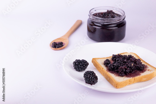 Plate with toast slice and berry jam, fresh blackberry and wooden spoon on pink background. Healthy breakfast concept top view, flat lay image. photo