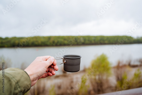 Coffee mug for camping in nature, man hand holding a mug, tea glass, metal cup for hot drinks, aluminum utensils