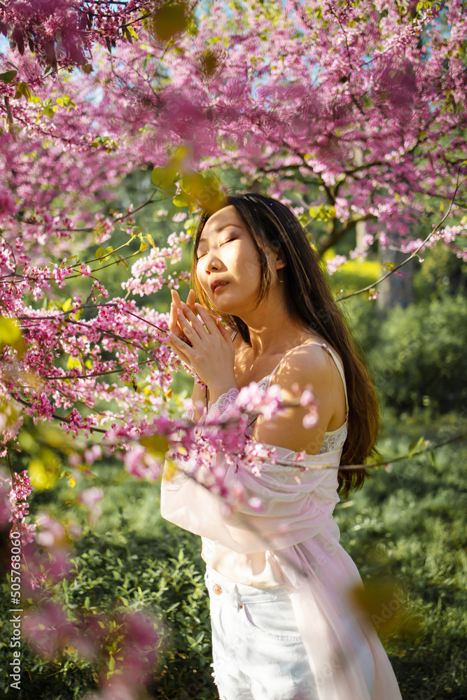 Outdoor portrait of beautiful young Chinese girl among blossom cherry tree brunch in spring garden, beauty, summer, emotion, expression and people concept.