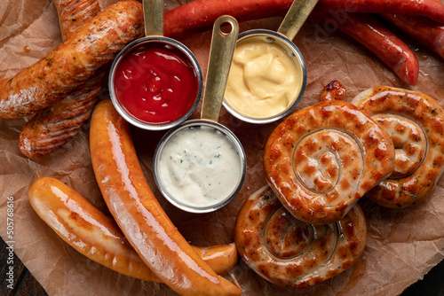 A mix of grilled sausages - Bavarian, round, Cumberland, bratwurst with ketchup and sauce on a wooden table. German sausage menu, top view photo