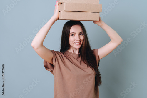Young pretty beautiful joyful woman holding above her head a stack of boxes carrying them