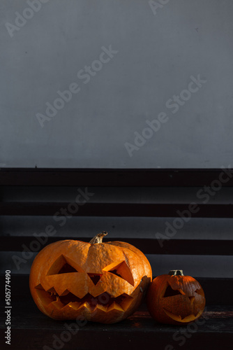 Two scary Halloween pumpkins on a bench by the wall at evening. Happy Halloween