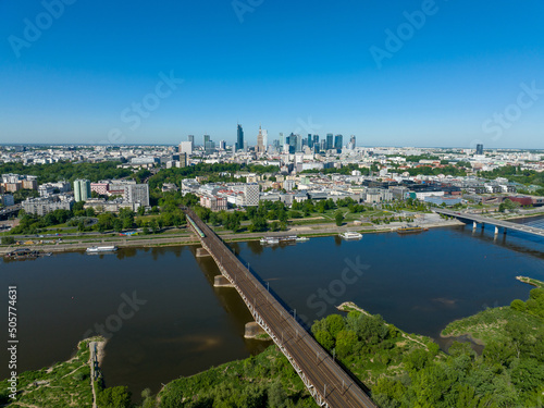 Widok na cenrum Warszawy z lotu ptaka z drona, widoczny most kolejowy oraz most Świętokrzyski, wiosna, dużo zieleni i niebieskie niebo