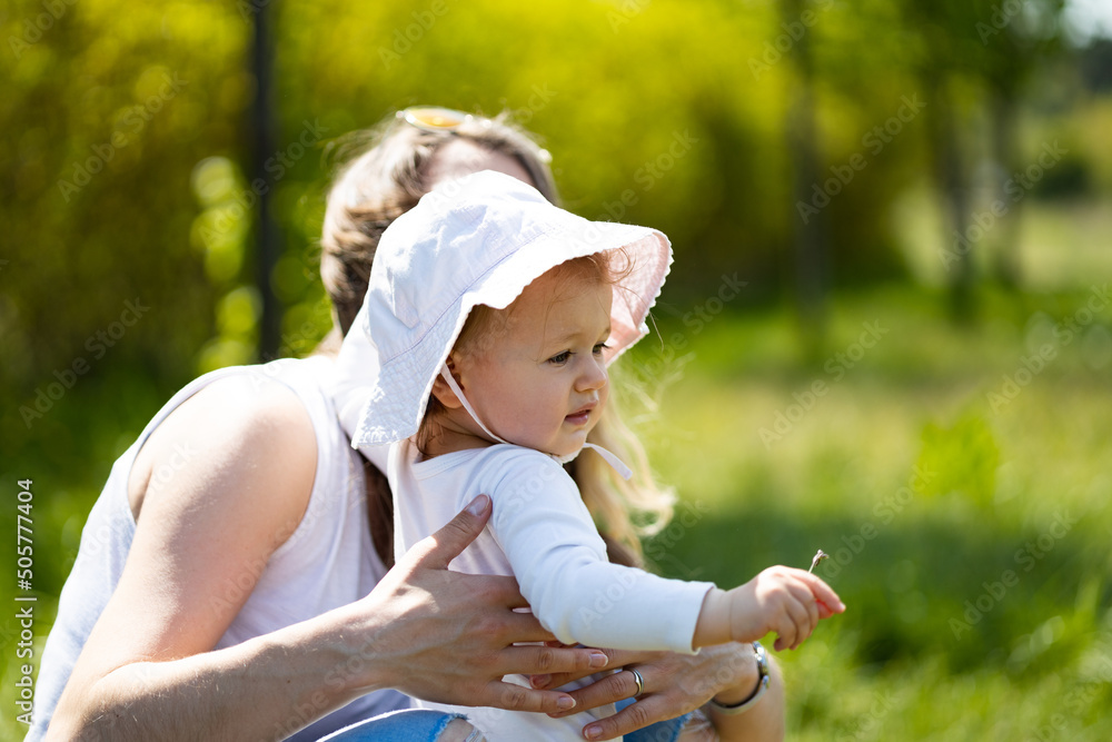 mother holds baby girl with white hat at sunny summer day, outdoor fun - obrazy, fototapety, plakaty 