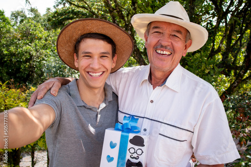 Father and son taking a selfie on father's day. Latino family in sombrero and farm work clothes.