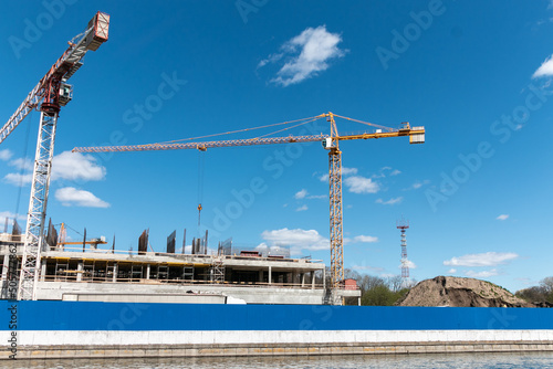Construction cranes at a construction site in the city against the blue sky. The concept of building a new area. Construction of a new building.