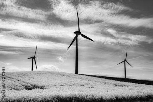 windmills from a wind farm against a blue sky and yellow rape