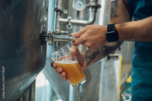 Close shot of a man filling glass of beer on a tap in brewery