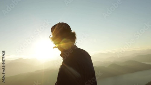 View of the silhouette of a man, contemplating the landscape from the top of the hill, at sunset. View of the mountains and sun, creating a beautiful lens flare. 