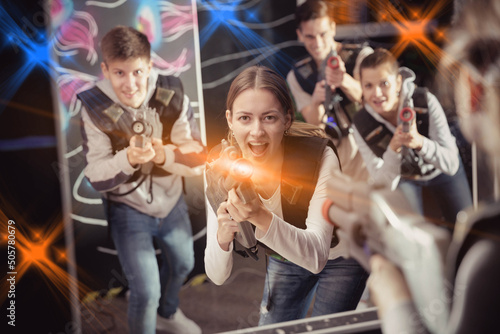 Excited girl aiming laser gun at other players during lasertag game in dark room