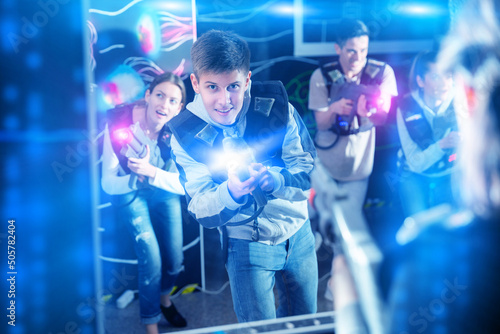 Portrait of happy young man with laser pistol and playing laser tag with his friends in dark room. High quality photo © JackF