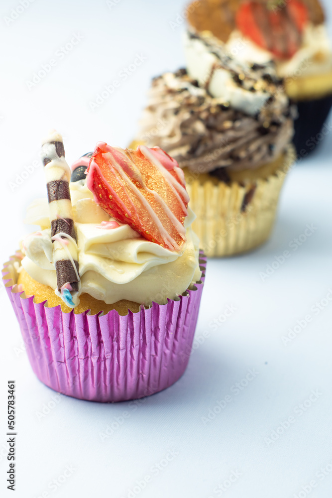 Beautiful muffin cupcakes decorated with fruits, chocolate, golden sprinkles, and cookies, in one line. Many pastries on light background.