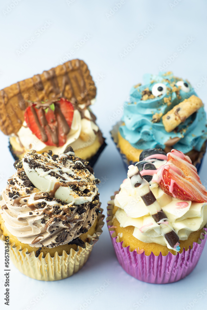 Colorful, funny and delicious muffin cupcakes collection decorated in various styles. Pastries with cream, fruits, cookies and chocolate on light blue background.