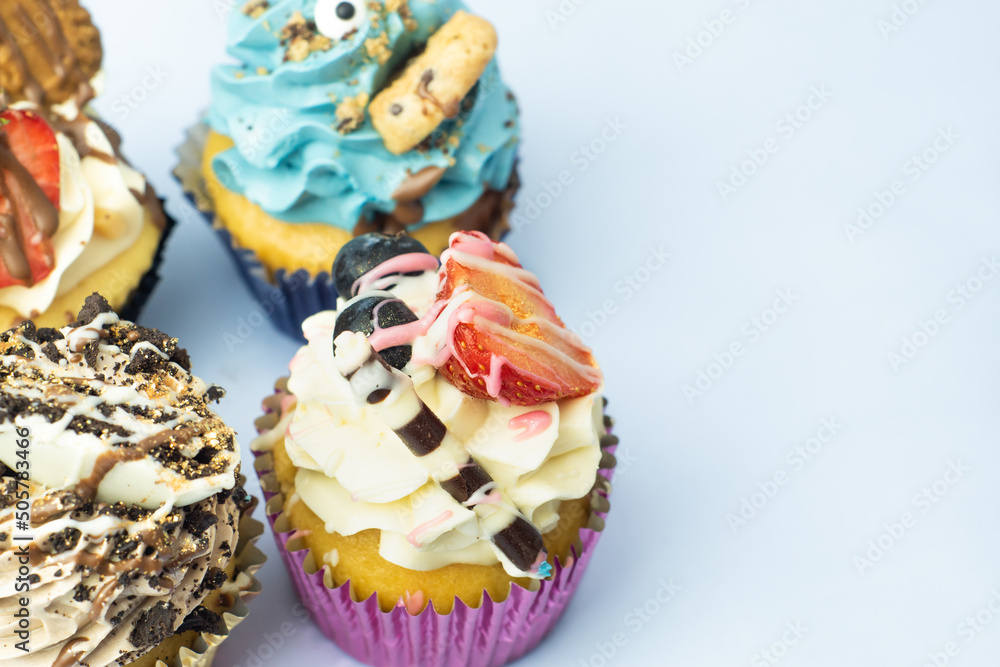 Colorful, funny and delicious muffin cupcakes collection decorated in various styles. Pastries with cream, fruits, cookies and chocolate on light blue background.