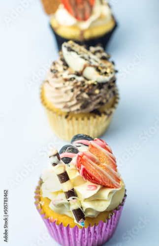 Obraz na płótnie Beautiful muffin cupcakes decorated with fruits, chocolate, golden sprinkles, and cookies, in one line. Many pastries on light background. w salonie