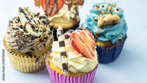 Obraz na płótnie Colorful, funny and delicious muffin cupcakes collection decorated in various styles. Pastries with cream, fruits, cookies and chocolate on light blue background. w salonie