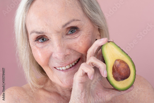 Studio portrait of smiling senior woman holding halved avocado photo