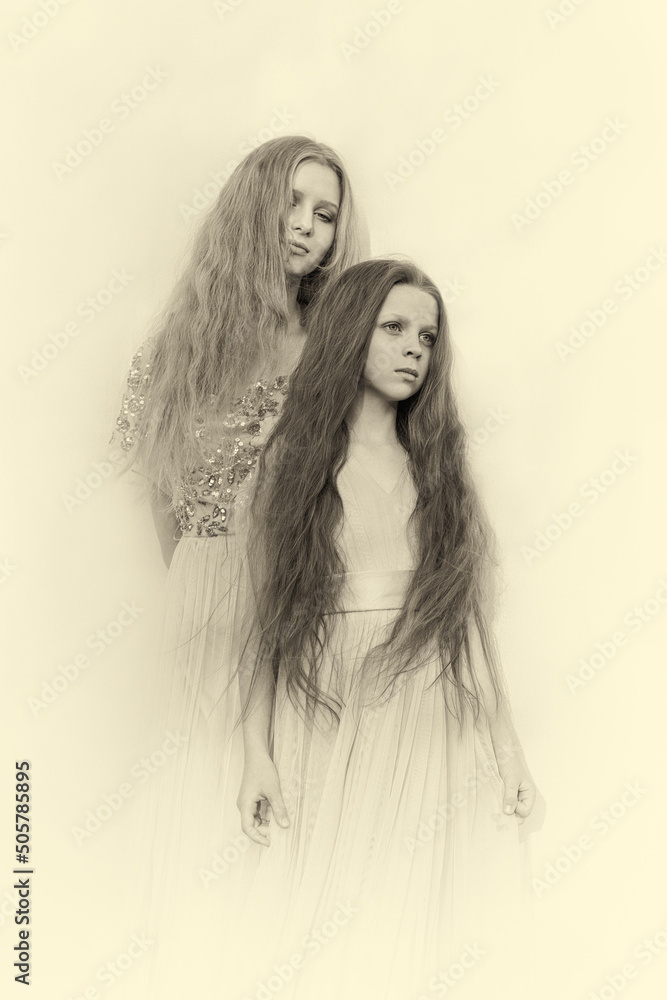 Two Sisters with long hair in beautiful dresses on a light background. Retro photo. Sepia. Attractive two young Girls posing for the camera. Girls with long hair. Beautiful models. Beautiful Sisters. Two Sisters with long hair in beautiful dresses on a light background. Retro photo. Sepia. Attractive two young Girls posing for the camera. Girls with long hair. Beautiful models. Beautiful Sisters.