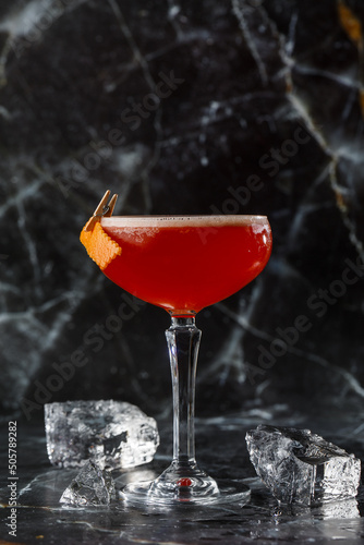 A red sour cocktail in a coupe glass garnished with an orange peel. Clover club with imported gin.