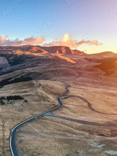 Aerial view of mountain road and beautiful orange sunrise in autumn. Top view of mountain landscape