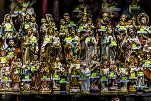 Concept of belief and religion - a close-up of a souvenir shop window with figures of saints with price tags visible.