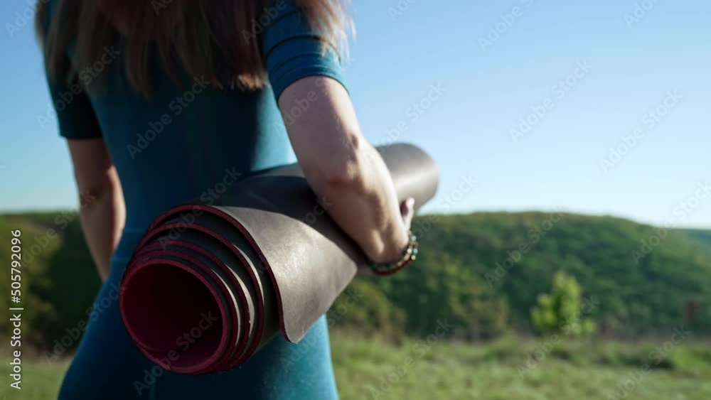 Young woman walking to do morning yoga practice. Active girl holding fitness mat, sports equipment. Green grass, nature background. Summer day. Young woman walking to do morning yoga practice. Active girl holding fitness mat, sports equipment. Green grass, nature background. Summer day.