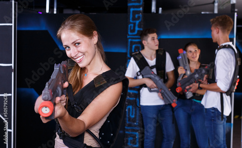 Smiling girl with laser pistol during playing laser tag with her friends in dark room.