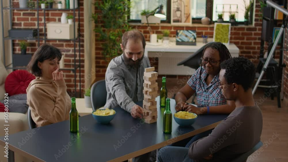 Young man losing game and destroying wooden tower cubes, having fun with building construction blocks and square pieces on table. Smiling people enjoying funny leisure activity. Young man losing game and destroying wooden tower cubes, having fun with building construction blocks and square pieces on table. Smiling people enjoying funny leisure activity.