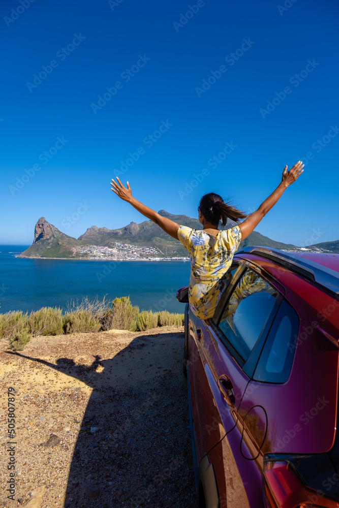 Φωτογραφία woman outside car window road trip with hands up, car at Chapmans Peak Drive in Cape Town South Africa looking out over the ocean