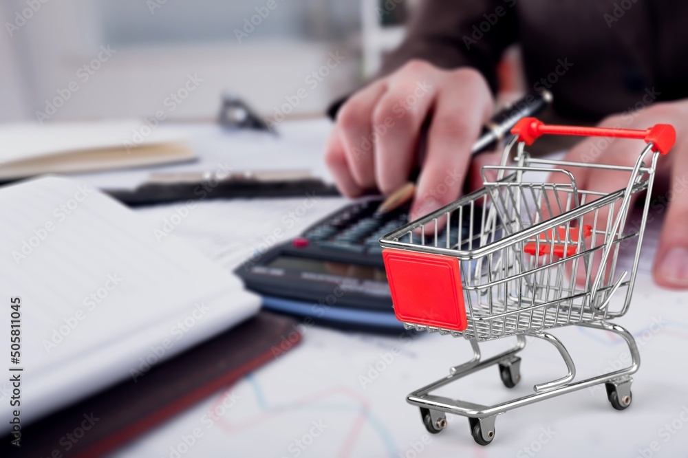 Shopping cart and man working on calculator with financial document. Financial crisis concept. Shopping cart and man working on calculator with financial document. Financial crisis concept.