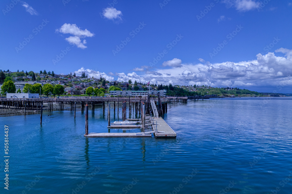 An empty boat tied to a wooden dock floats on the Puget Sound under a cloudy blue sky at Commencement Bay in Tacoma, Washington.