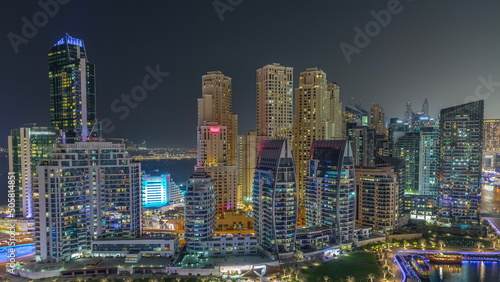 Dubai Marina with several boats parked near waterfront and skyscrapers around canal aerial night timelapse.