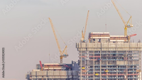 High buildings under construction and many yellow cranes in downtown timelapse at evening during sunset. Active work at construction site of new towers and skyscrapers. photo