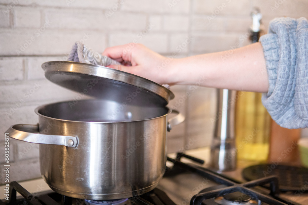 woman checking the pot on the stove boiling water