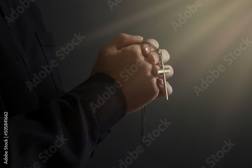 Obraz na płótnie Holy light and priest with cross praying on black background, closeup