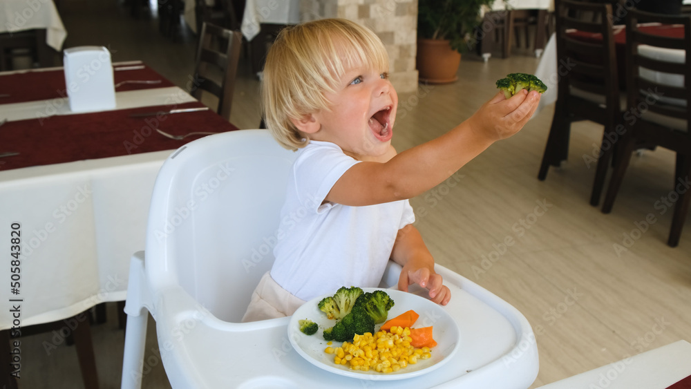 little boy holds broccoli in his hand and stretches forward