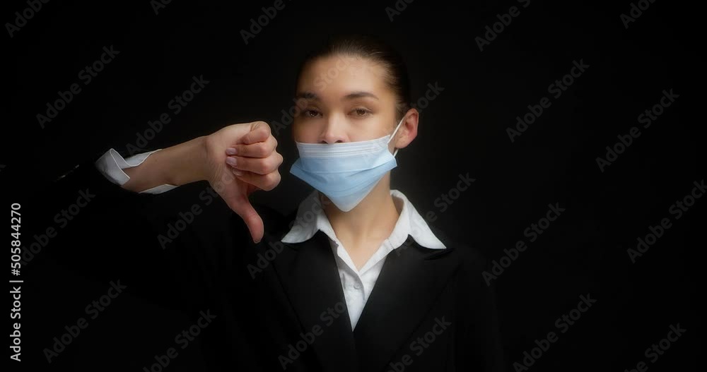 An Asian woman in business clothes shows a video instruction on how to properly wear a medical mask during an pandemic, flu, coronavirus. Thumb down, thumb up, isolated on black background An Asian woman in business clothes shows a video instruction on how to properly wear a medical mask during an pandemic, flu, coronavirus. Thumb down, thumb up, isolated on black background