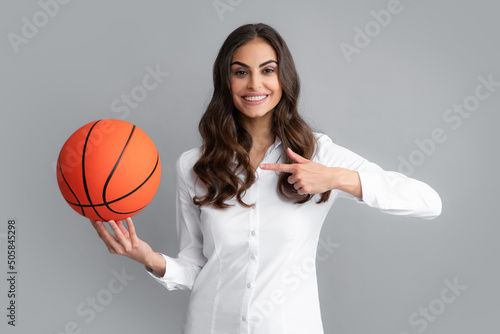 Happy woman pointing finger on basketball ball, isolated on gray background. © Olena
