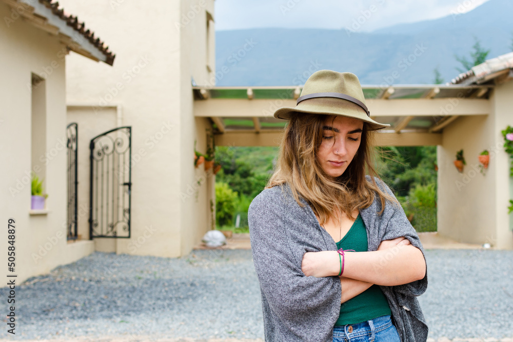 Young woman wearing a hat with a melancholy expression with colonial architecture in the background