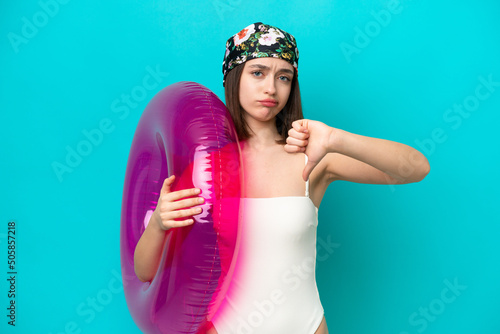 Young Ukrainian woman holding air mattress isolated on blue background showing thumb down with negative expression