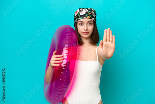 Young Ukrainian woman holding air mattress isolated on blue background making stop gesture