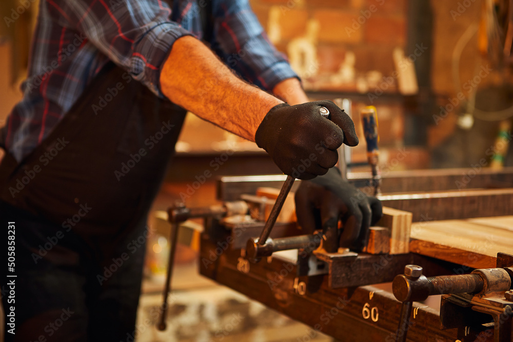 Portrait of a senior carpenter in uniform gluing wooden bars with hand pressures at the carpentry manufacturing Portrait of a senior carpenter in uniform gluing wooden bars with hand pressures at the carpentry manufacturing