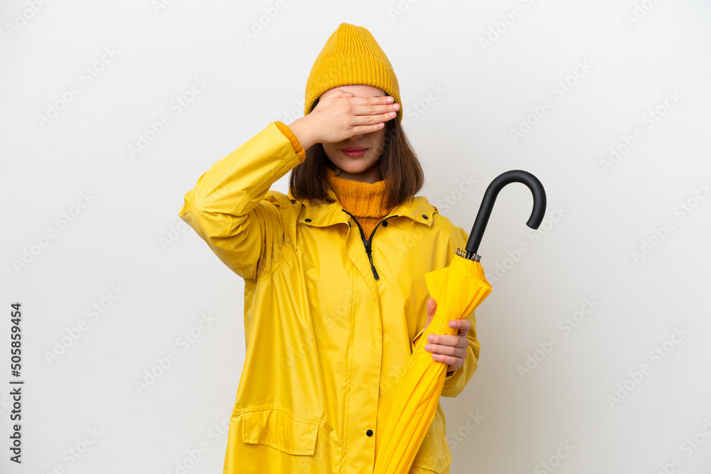 Young Ukrainian woman with rainproof coat and umbrella isolated on white background covering eyes by hands. Do not want to see something Young Ukrainian woman with rainproof coat and umbrella isolated on white background covering eyes by hands. Do not want to see something